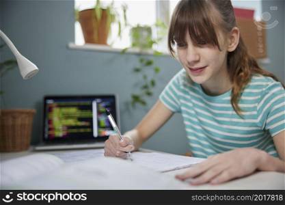 Teenage Girl Doing Homework At Desk In Bedroom