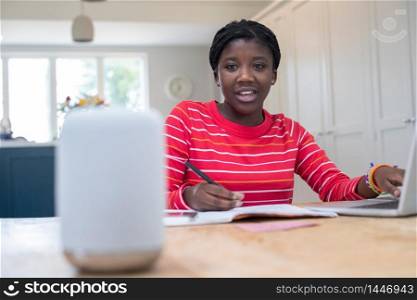 Teenage Girl Doing Homework At Home Asking Digital Assistant Question
