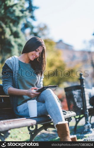 Teenage girl drinking coffe and using digital tablet in park