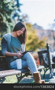 Teenage girl drinking coffe and using digital tablet in park