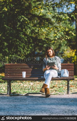 Teenage girl drinking coffe and using digital tablet in park