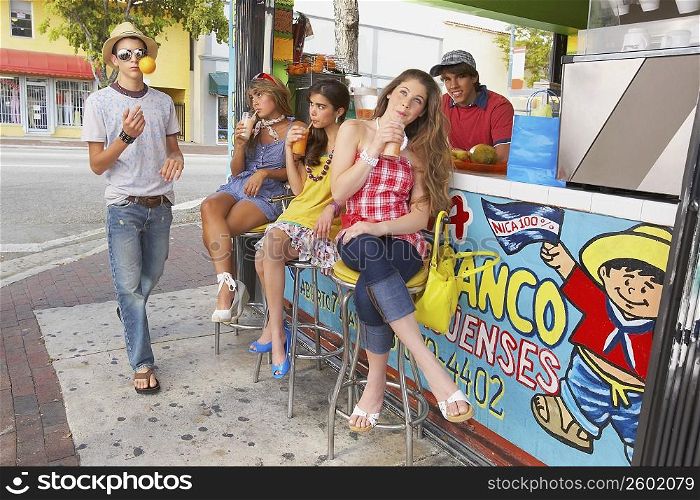 Teenage girl drinking juice with her two friends and a teenage boy tossing a lemon in front of them