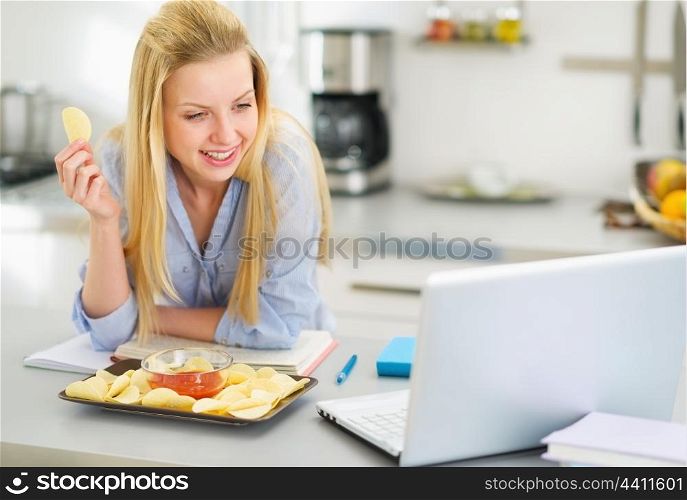 Teenage girl eating chips and looking in laptop