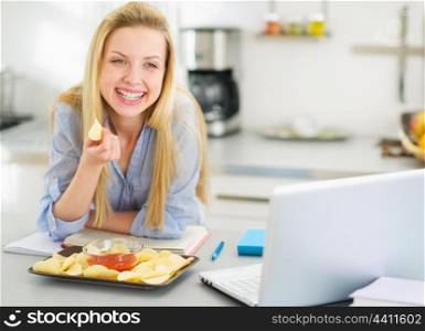 Teenage girl eating chips while studying in kitchen