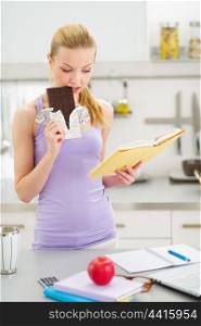 Teenage girl eating chocolate while studying in kitchen