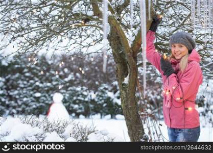 Teenage Girl Hanging Fairy Lights In Tree With Icicles In Foreground