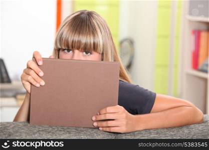 Teenage girl hiding behind a book.