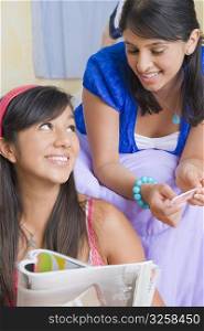 Teenage girl holding a magazine with a young woman lying on the bed beside her