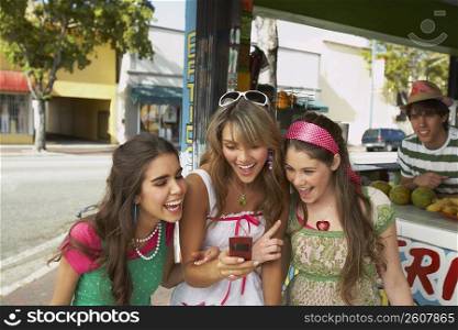 Teenage girl holding a mobile phone and standing at a juice bar with her friends