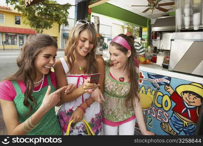 Teenage girl holding a mobile phone and standing at a juice bar with her friends