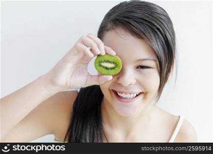 Teenage girl holding a slice of kiwi fruit in front of her eye