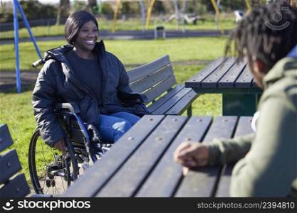 Teenage Girl In Wheelchair Hanging Out Talking And Laughing With Friends In Park