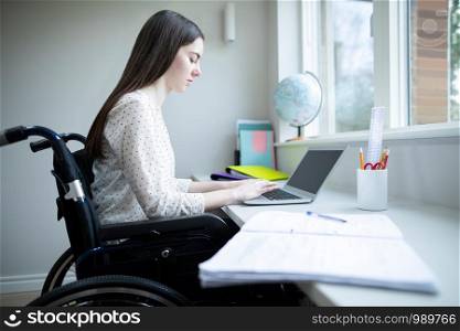 Teenage Girl In Wheelchair Studying At Home On Laptop