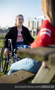 Teenage Girl In Wheelchair Talking With Friend In Park