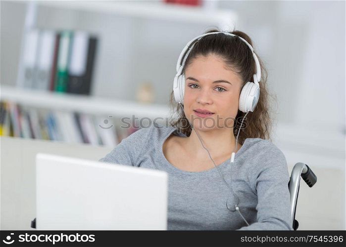 Teenage girl in wheelchair wearing headphones and using laptop