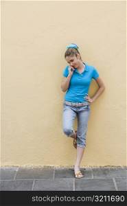 Teenage girl leaning against a wall and talking on a mobile phone