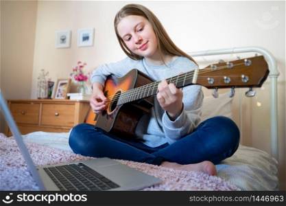 Teenage Girl Learning To Play Acosutic Guitar With Online Lesson On Laptop Computer