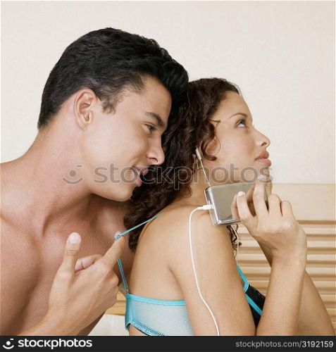 Teenage girl listening to an MP3 player with a young man sitting behind her