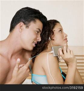 Teenage girl listening to an MP3 player with a young man sitting behind her