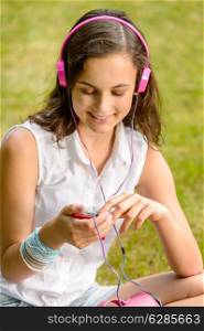 Teenage girl listening to music with headphones sitting on grass