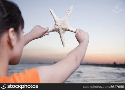 Teenage girl looking and holding up starfish
