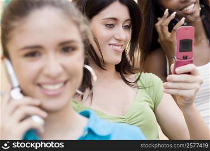 Teenage girl looking at a mobile phone with two other teenage girls talking on mobile phones