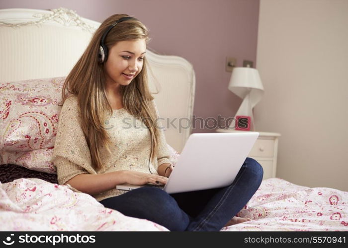 Teenage Girl Lying On Bed Using Laptop Wearing Headphones