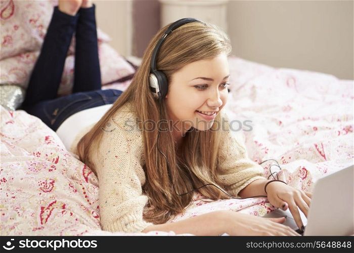 Teenage Girl Lying On Bed Using Laptop Wearing Headphones