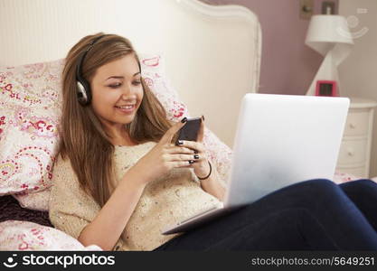 Teenage Girl Lying On Bed Using Laptop Whilst Texting