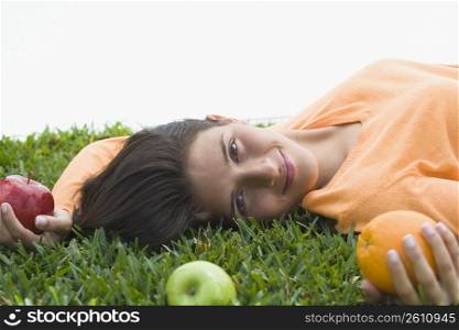 Teenage girl lying on grass and holding fruits