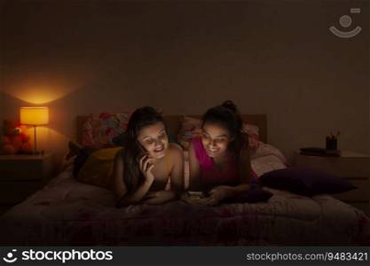 Teenage girl lying on her bed and talking on the phone while other texts on her mobile. 
