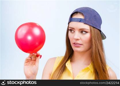 Teenage girl making funny silly faces. Young trendy woman in jeans cap holding red balloon.. Teenage girl with red balloon.
