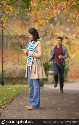 Teenage Girl Making Mobile Phone Call With Boyfriend Running Towards Her In Background