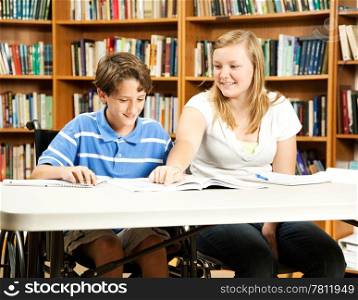 Teenage girl mentoring a younger, disabled boy in the school library.