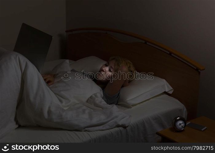 Teenage girl on laptop computer while in bed. Teen surrounded by technology even late at night. Selective lighting and focus on face.