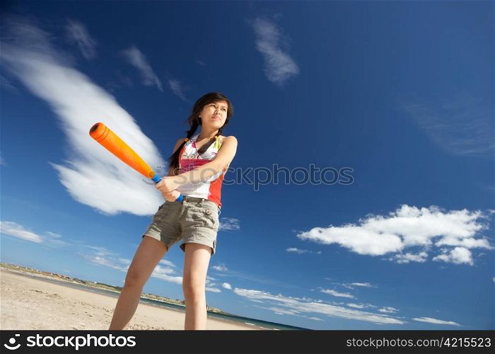 Teenage girl playing baseball on beach