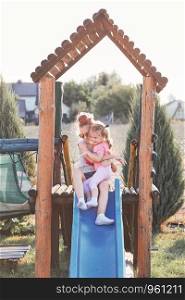 Teenage girl playing with her younger sister in a home playground in a backyard. Happy smiling sisters having fun on a slide together on summer day. Real people, authentic situations