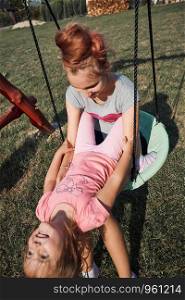 Teenage girl playing with her younger sister in a home playground in a backyard. Happy smiling sisters having fun on a swing together on summer day. Real people, authentic situations