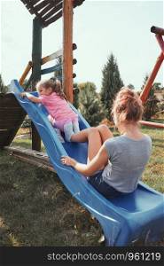 Teenage girl playing with her younger sister in a home playground in a backyard. Happy smiling sisters having fun on a slide together on summer day. Real people, authentic situations