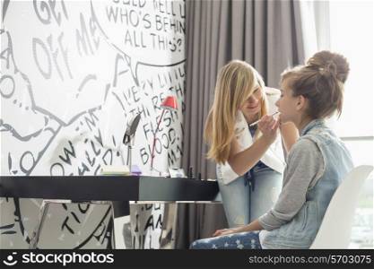 Teenage girl putting lipstick on sister at home