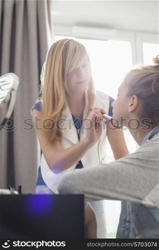 Teenage girl putting makeup on sister at home