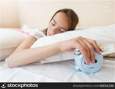Teenage girl putting ringing alarm clock under the pillow