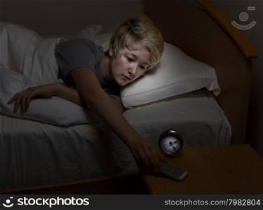 Teenage girl reaching for her cell phone, on night stand, while in bed. Teen using technology late at night instead of sleeping.