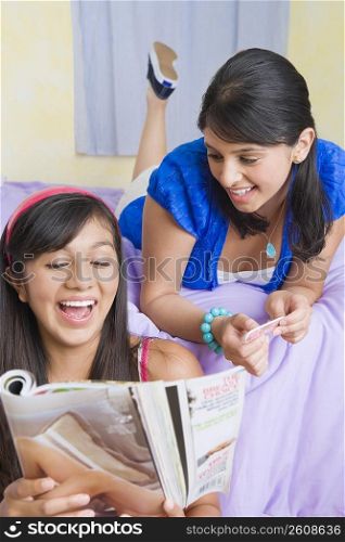 Teenage girl reading a magazine with a young woman lying on the bed behind her