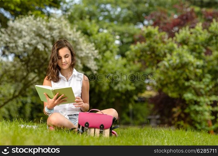 Teenage girl reading book sitting on grass summer park
