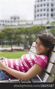 Teenage girl reclining on a bench in a park