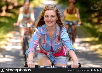 Teenage girl riding bike with friends on countryside road