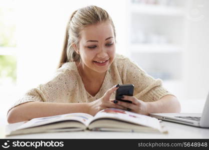 Teenage Girl Sending Text Message Whilst Studying On Laptop