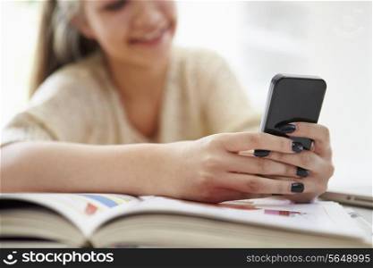 Teenage Girl Sending Text Message Whilst Studying On Laptop