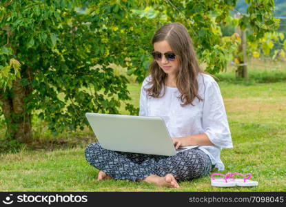 teenage girl sitting in the grass using a laptop